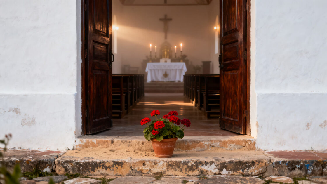 Puertas de madera abiertas de una iglesia de pueblo por la mañana, con una maceta de geranios en el escalón