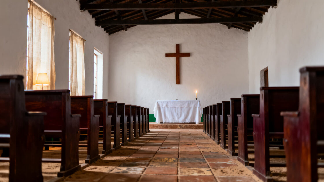 La nave vacía de una iglesia de pueblo vista entre los bancos, con el altar de lino blanco al fondo, por la mañana