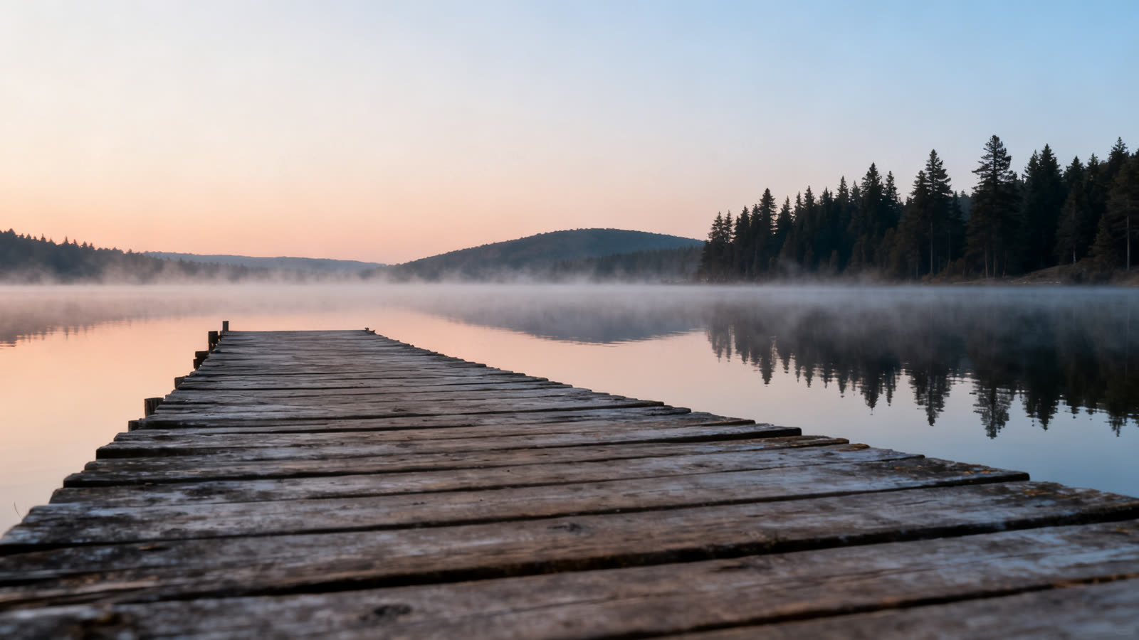 Un muelle de madera sobre un lago en calma al amanecer, con neblina suave sobre el agua